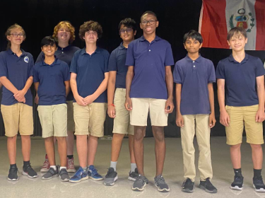  Several students in blue collared shirts and khaki bottoms stand in a line.
